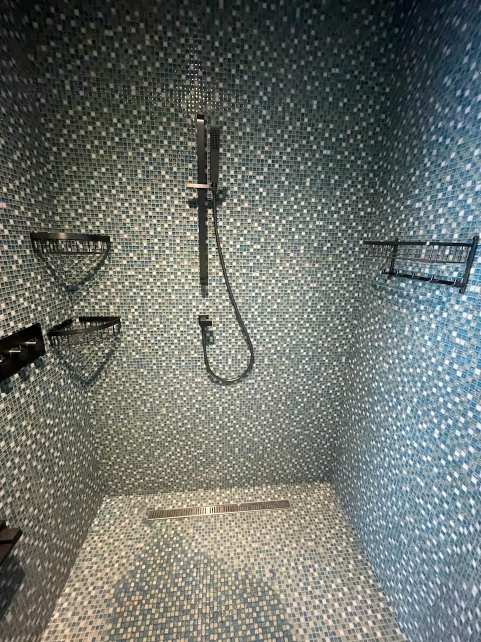 Walk-in shower lined in blue and white glass mosaic tiles, with a linear drain and dark shower fittings