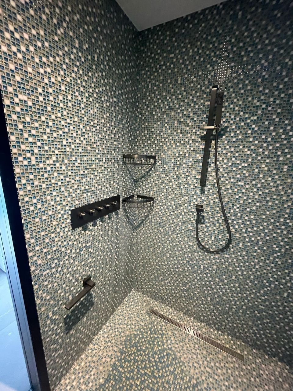 Mosaic-tiled shower with concealed controls, corner shelves, a riser rail and a linear drain