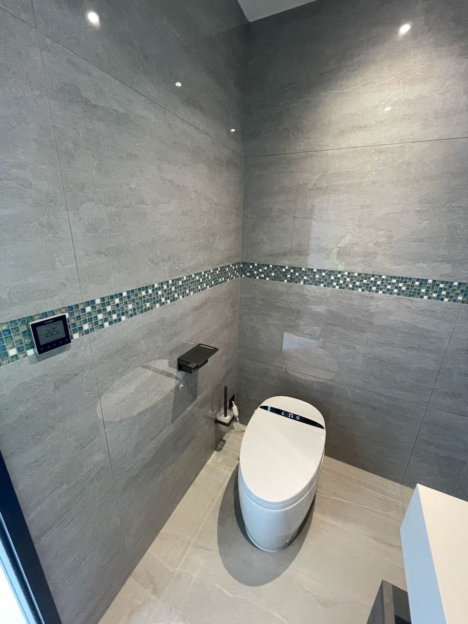 Smart WC and wall control panel in a bathroom with large grey porcelain tiles and a glass mosaic band