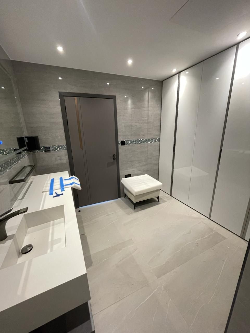 Bathroom with a long white basin, full-height gloss storage and a dark door set in grey tiled walls