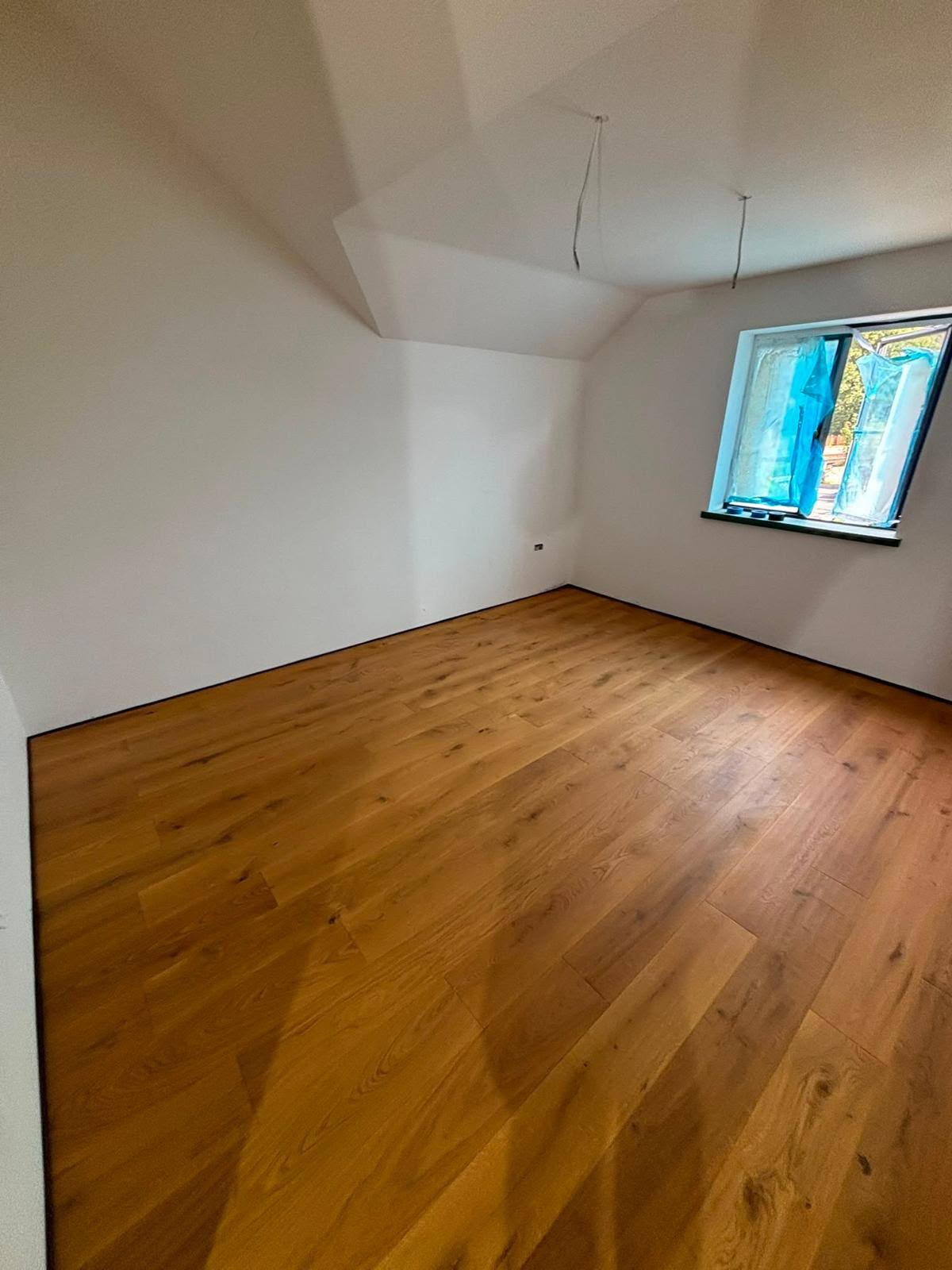Oak floorboards running into the corner of a room with a sloped ceiling and casement window