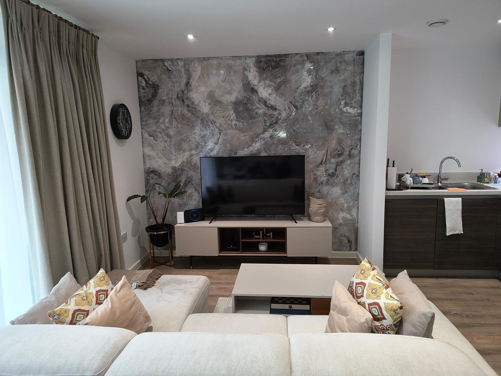 Living room with a marble-effect feature wall, recessed ceiling lights and an open kitchen beyond