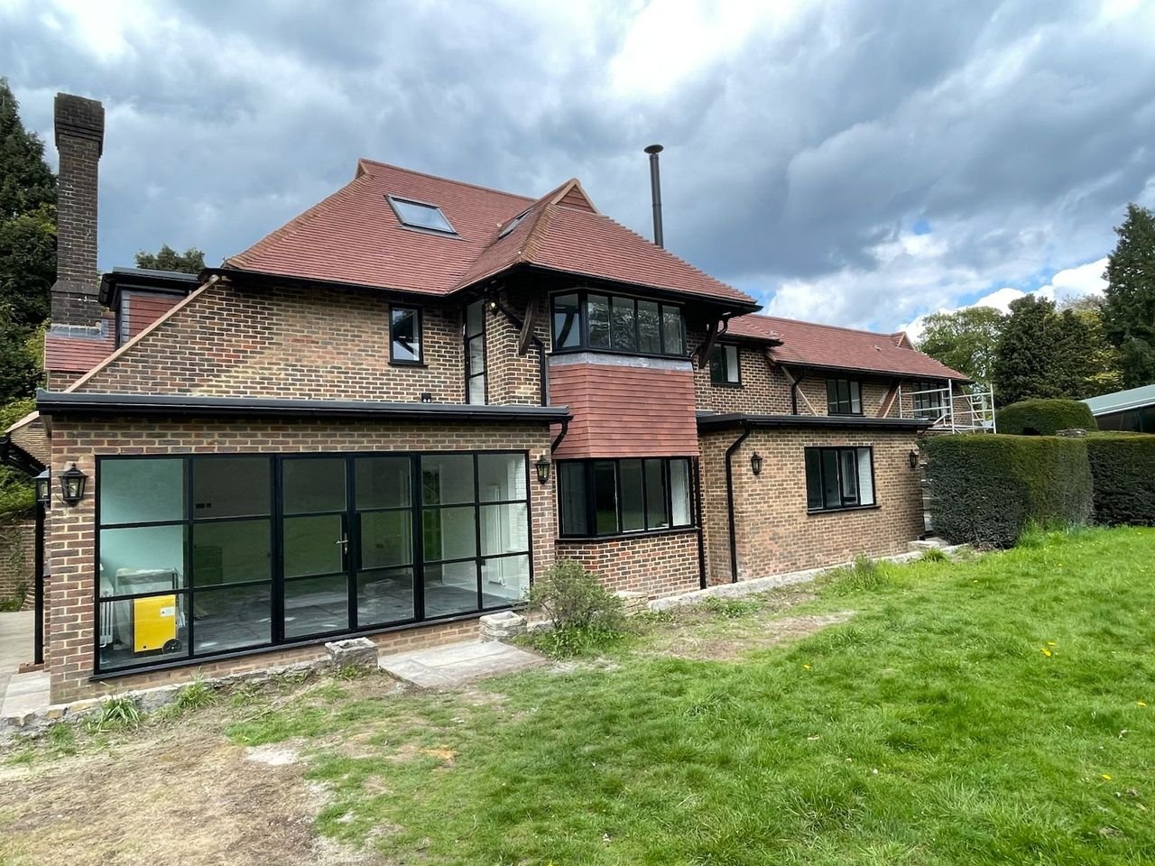 Two-storey brick house with a tall chimney, rooflights and wide black-framed glazing at ground floor