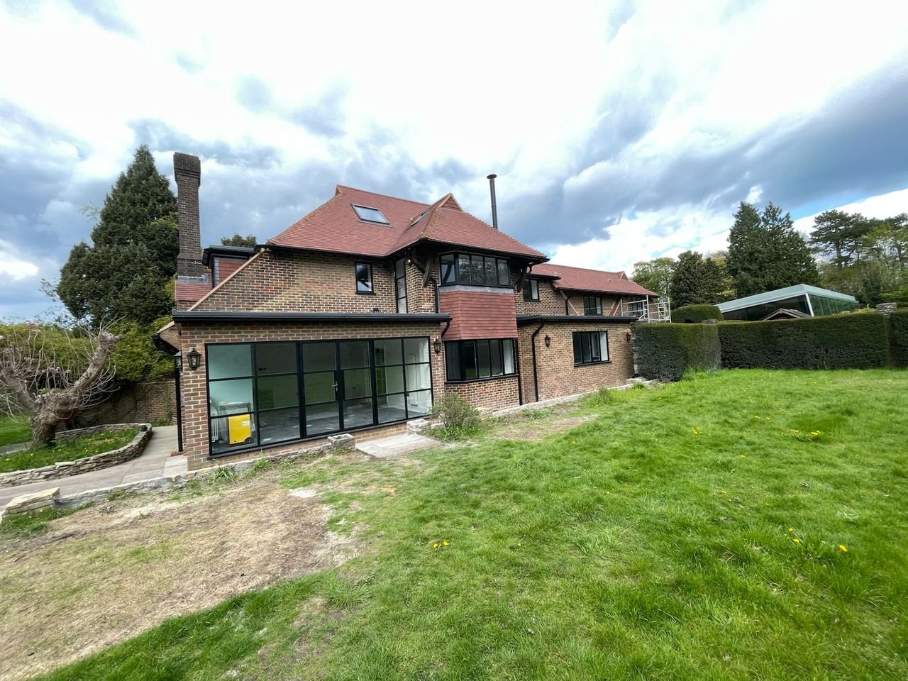 Rear of a brick and clay tile house with steel-framed glazed doors, viewed across the garden