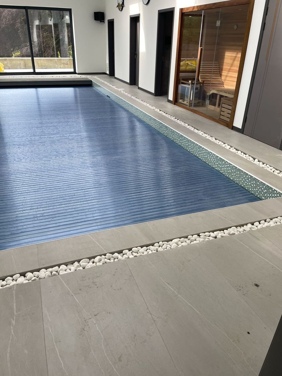 Porcelain-tiled pool surround with a white pebble channel beside a covered indoor pool