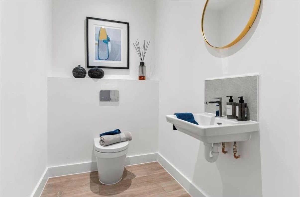 Cloakroom with a wall-hung basin, WC, round brass-framed mirror and wood-effect flooring