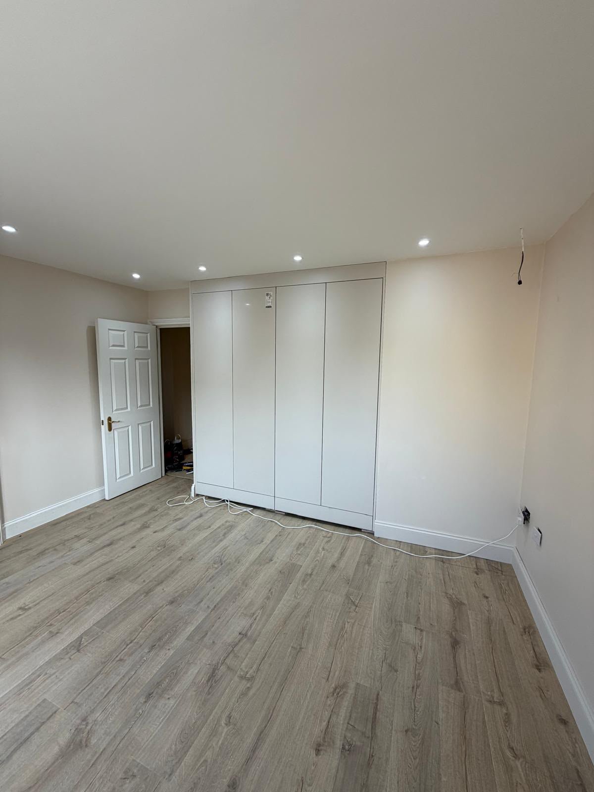 Refurbished bedroom with full-height fitted wardrobes, downlights and grey wood-effect flooring
