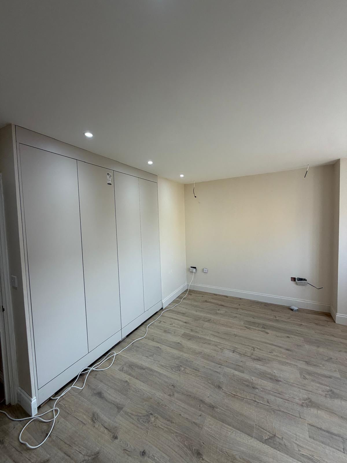 Wall of flush white fitted wardrobes in a newly refurbished room