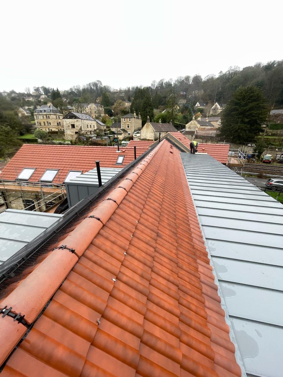 Clay tile ridge running alongside an aluminium roof section, looking out across a valley