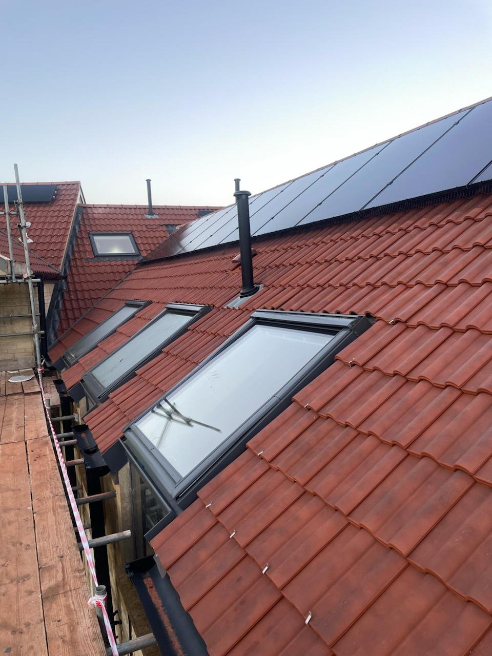 Pitched clay tile roof with a row of rooflights and solar panels, with scaffolding along the eaves