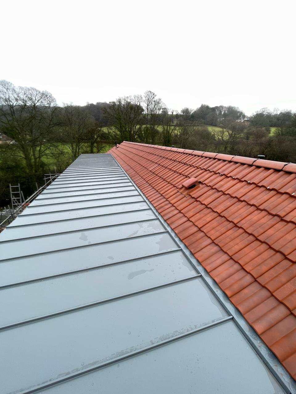 Standing seam aluminium roof meeting a pitched clay tile roof