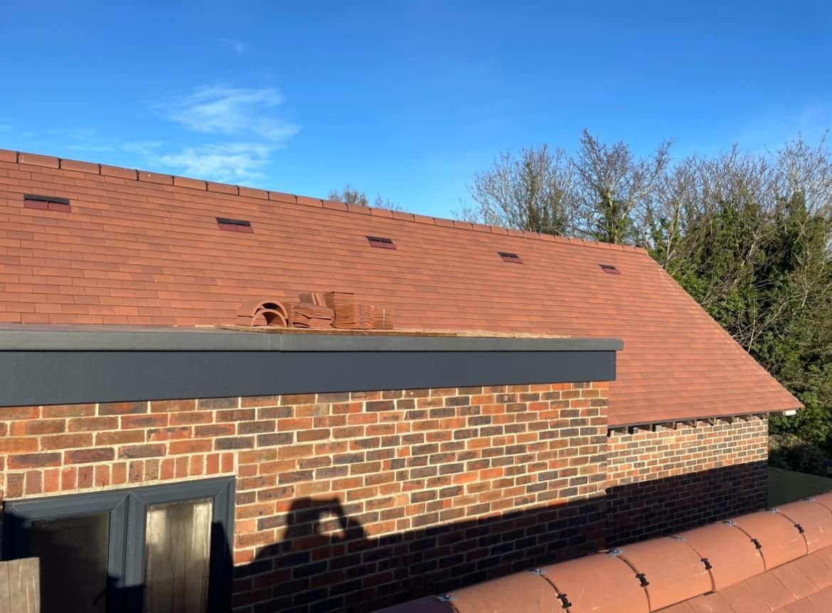 Newly tiled roof above a brick building with a dark fascia, under a clear blue sky