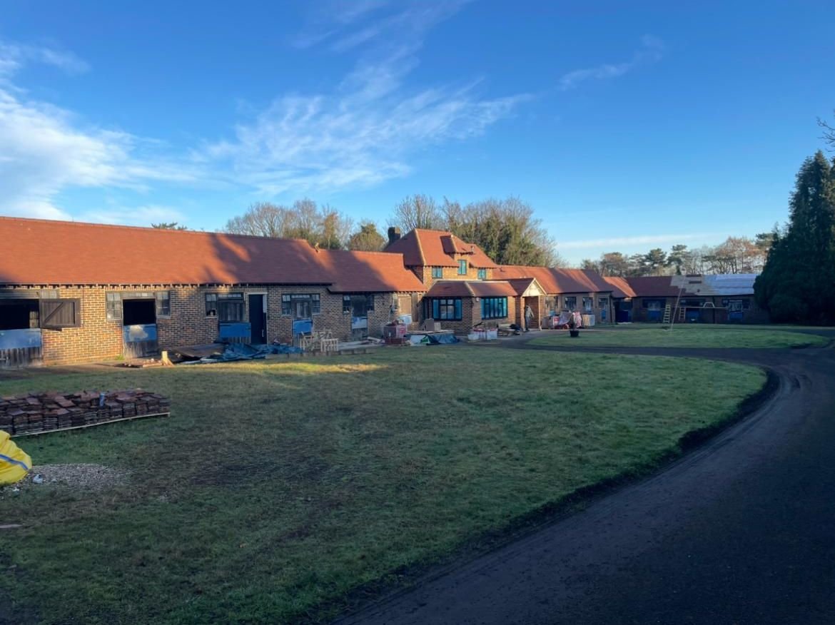 Long single-storey brick buildings with new clay tile roofs around a grassed courtyard