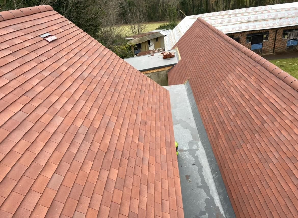 Two clay tile roof slopes meeting at a lined valley gutter, with further roofs beyond